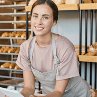 Bäckerin hält Tablet in der Hand, im Hintergrund sind Brötchen - Dienstplan Bäckerei 