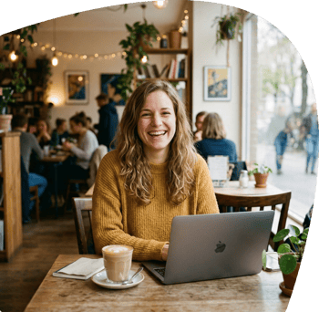 Frau sitzt lächelnd an Laptop in einem Cafe