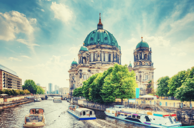 It is the Berlin Cathedral on the river Spree to see on a sunny summer day. There are several boats on the river Spree. 