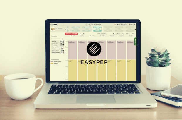 On a laptop you can see a timesheet with the easyPep logo. The laptop is placed on a charming workplace with a plant and coffee on the table.