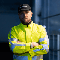 Sicherheitsmann mit neon-gelber Jacke guckt in die Kamera - Dienstplan Sicherheitsdienst