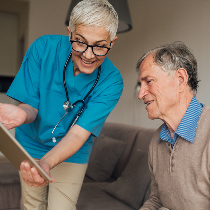 Pflegerin zeigt ihrem Patienten etwas auf einem Tablet und beide lächeln