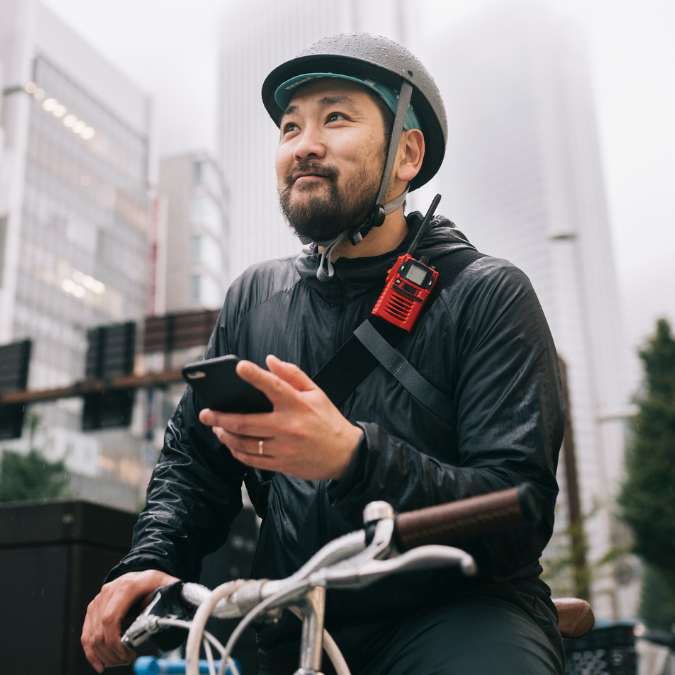 Lieferant steht neben seinem Fahrrad und hält ein Handy in der Hand und lächelt