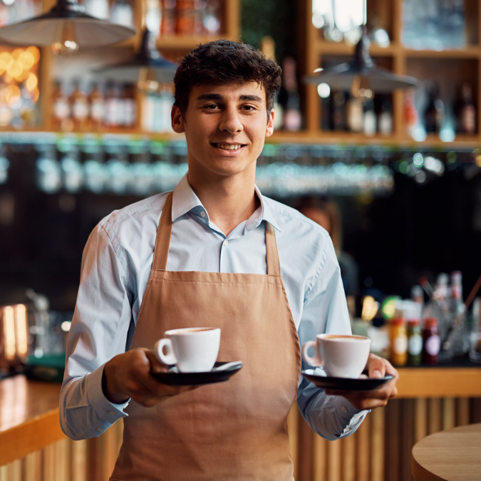 Junger Mann hält zwei Cafes in den Händen und lächelt