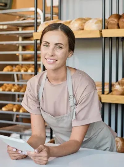 Lächelnde Bäckereimitarbeiterin in Schürze an der Theke vor Brotregalen